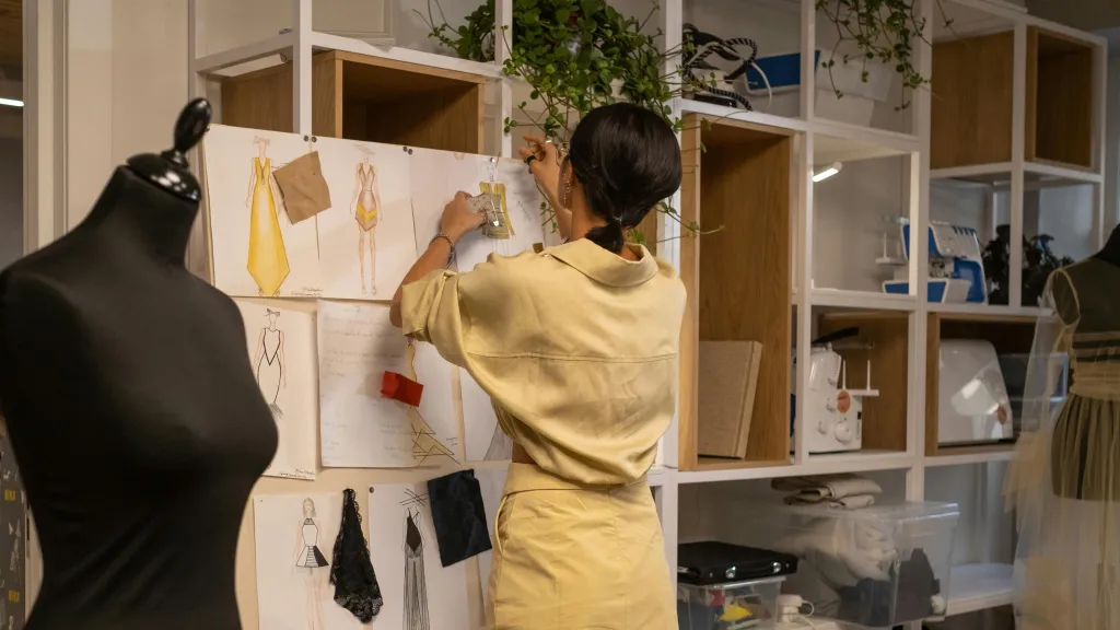 Woman with dark hair wearing yellow dress pinning fabric swatches on a board to illustrate article about advisors helping to grow small business.