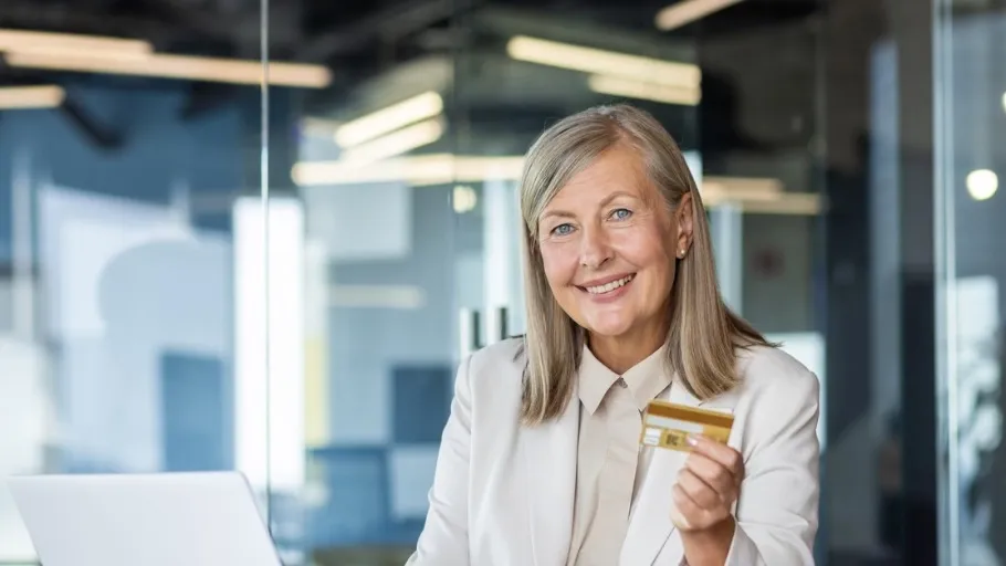 Woman wearing suit holding credit card smiling to illustrate article about 0% APR credit cards