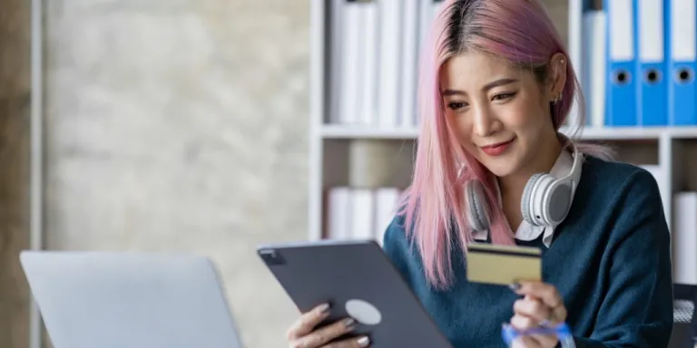 A woman small business owner sitting at a desk with her credit card and looking at an ipad for guidance on how to close a credit card