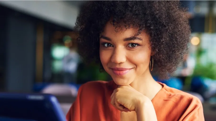 Woman with dark hair wearing orange short smiling in front of laptop to illustrate article about year end tax deductions.