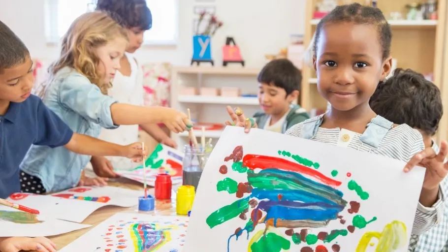 A young African-American girl holding up a painting of mixed colors at daycare