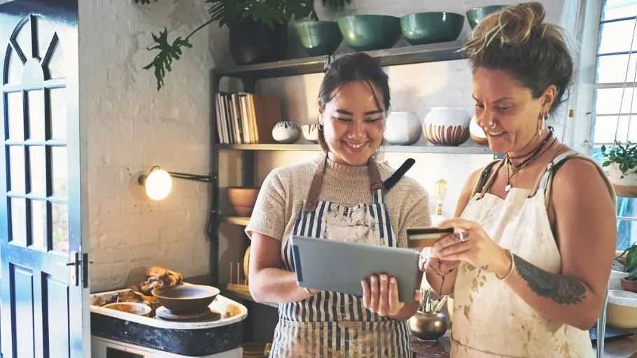 female small business owner holding a revenued business card and looking at an ipad with a co-worker