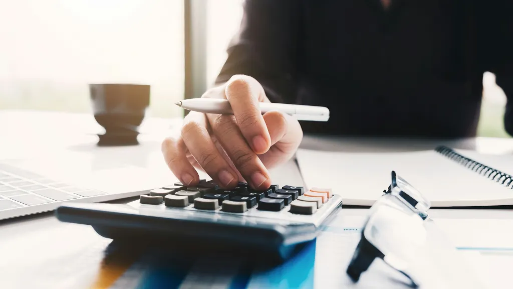 A person with a pen in hand uses a calculator