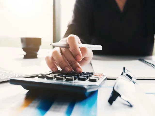 A person with a pen in hand uses a calculator