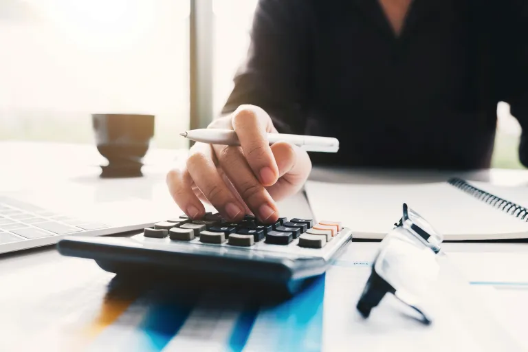 A person with a pen in hand uses a calculator