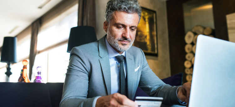 Handsome mature businessman with laptop in a hotel lounge. Man holding a credit card. Internet banking. Online payment.
