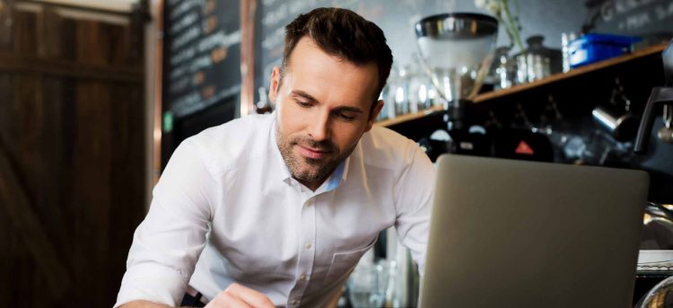 Happy cafe manager counting recipes with laptop