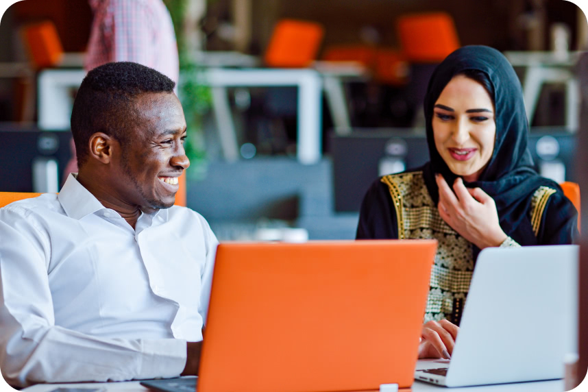 two people sitting next to each other with laptops, smiling and talking