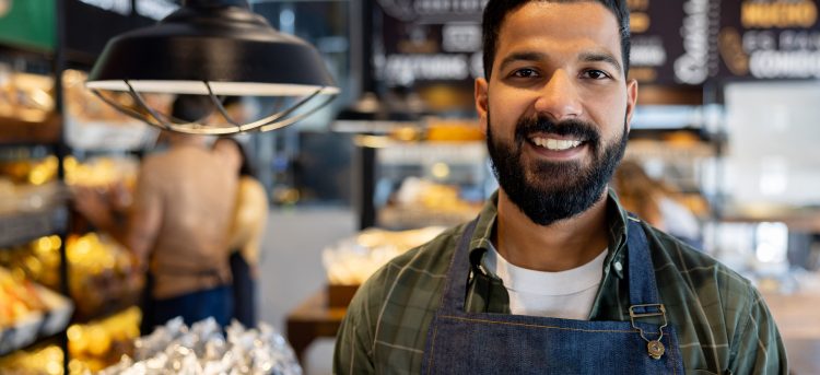 Portrait of a happy Indian business owner working at a bakery and looking at the camera smiling - food and drink establishment